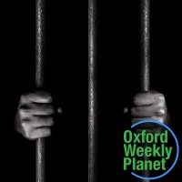 Hands gripping prison bars with the Oxford Weekly Planet logo in the foreground