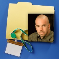 Manila folder with badge holder and lanyard with a photo of an unsmiling man with shaved head and close-shaved mustache and goatee