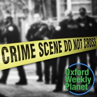 Police officers working behind yellow crime scene tape with the Oxford Weekly Planet logo in the foreground