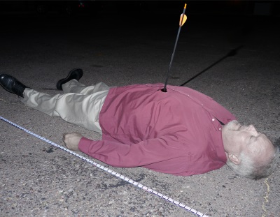 Man lying on his back on the asphalt with an arrow sticking out of his chest