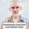 Older man with white hair, mustache and beard holding a jail booking card