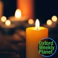 Candles burning on a dark background the Oxford Weekly Planet logo in the foreground