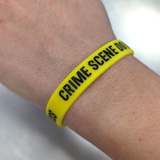 Person wearing a yellow wrist band printed with CRIME SCENE DO NOT CROSS